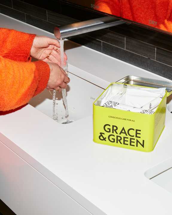 Person washing hands with Grace & Green product tin on the counter.